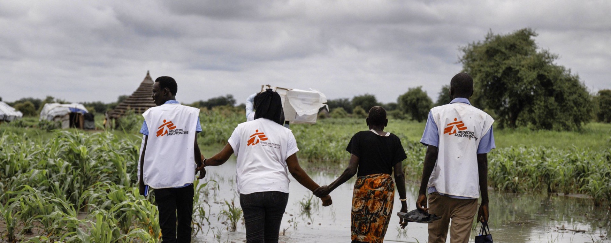 An MSF team walking through flooded farmland with a resident